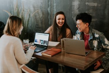 Drei Frauen sitzen um einen Tisch an ihren Laptops