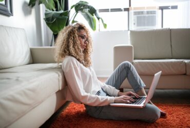 Frau sitzt mit Laptop auf dem Boden vor dem Sofa